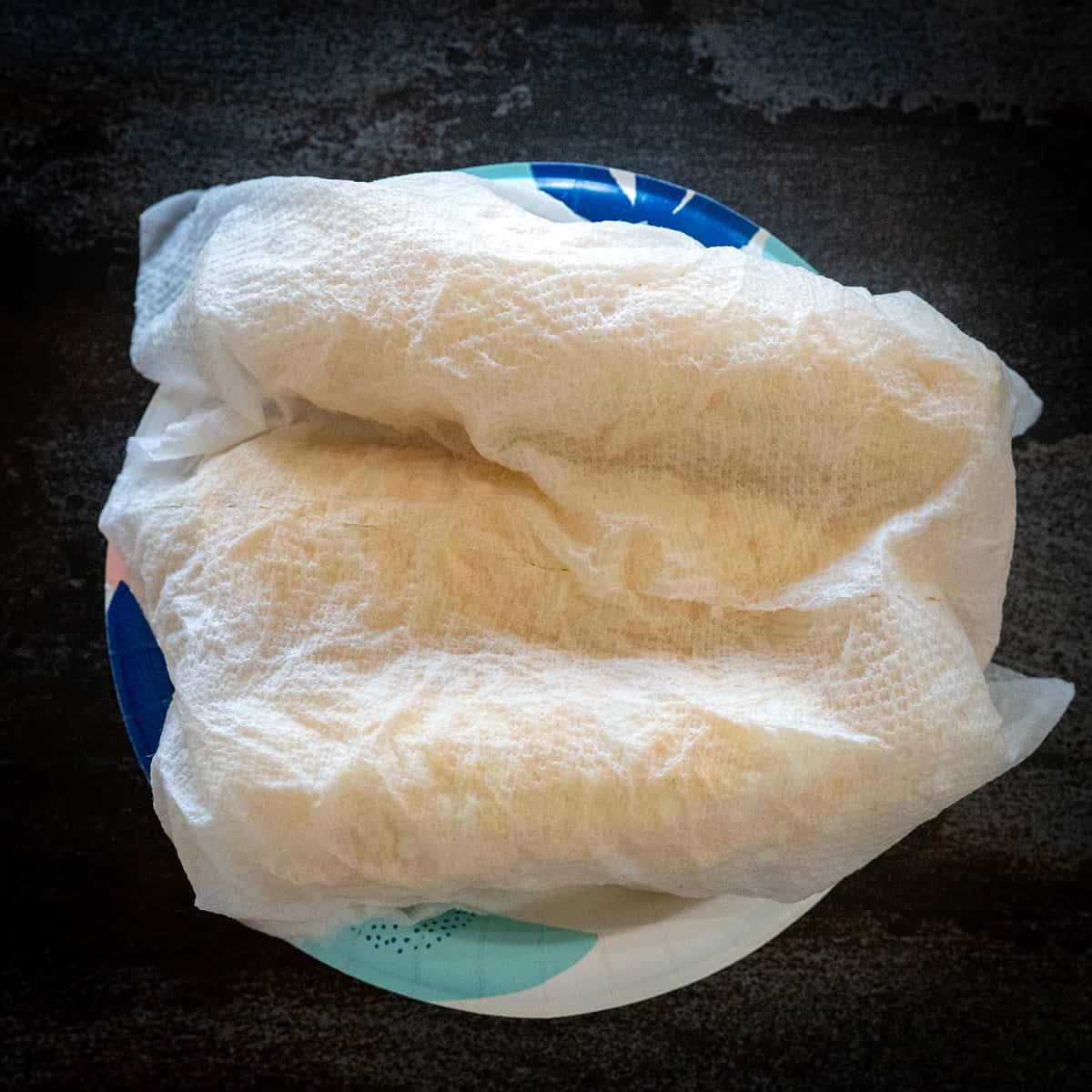 Corn cob wrapped in paper towel on plate.