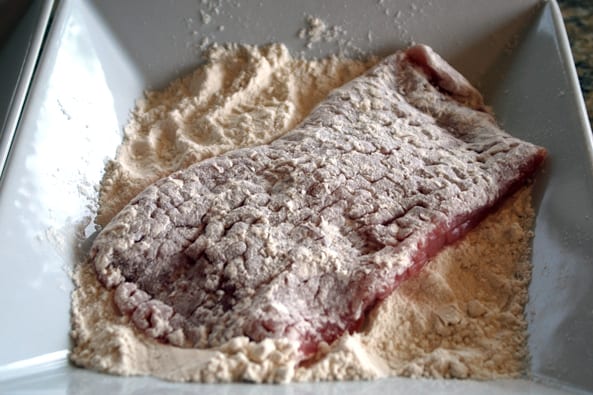 pork cutlet being dredged in flour