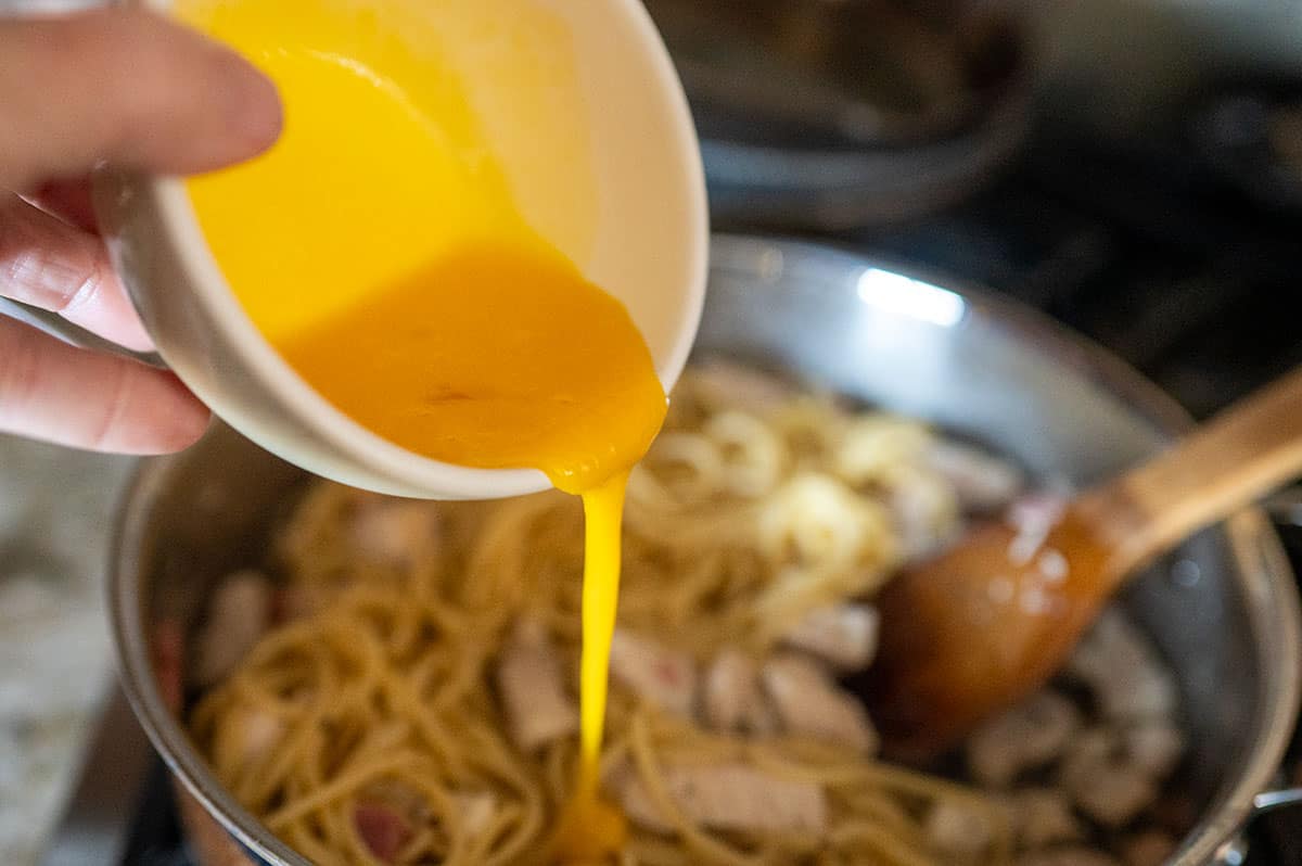 Pouring egg yolk into pasta.