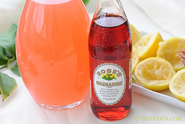 a bottle of grenadine syrup in front of a pitcher of pink lemonade