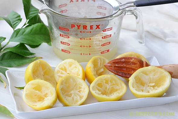 tray of juiced lemons with fresh lemon juice in a measuring cup