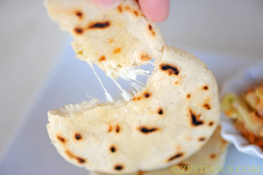 Pupusa being ripped open to reveal a cheesy center