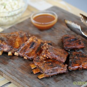 ribs with a side of sauce on a wooden cutting board