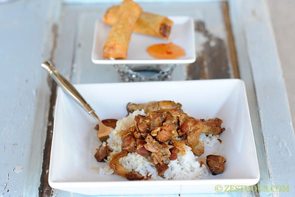 close up of chicken and pork adobo in a square bowl with a side of lumpia