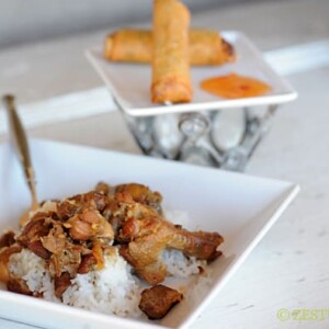 chicken and pork adobo in a square bowl with a side of lumpia