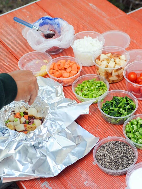 hand reaching in to add ingredients to foil packet.