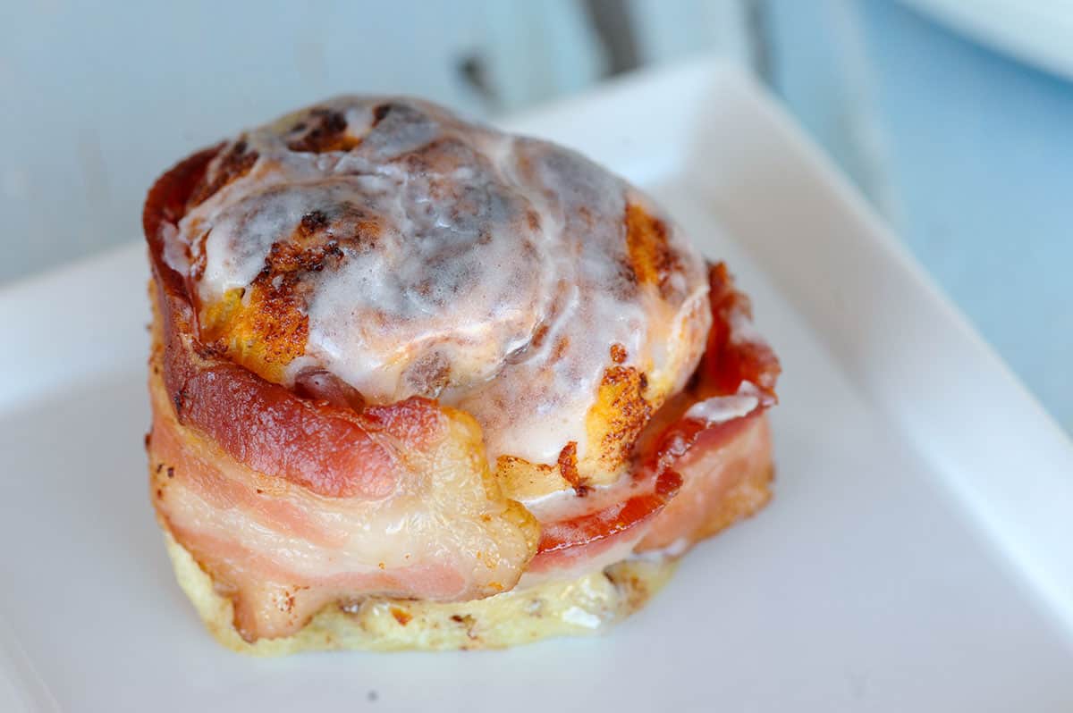 close up of bacon wrapped around baked cinnamon roll. 